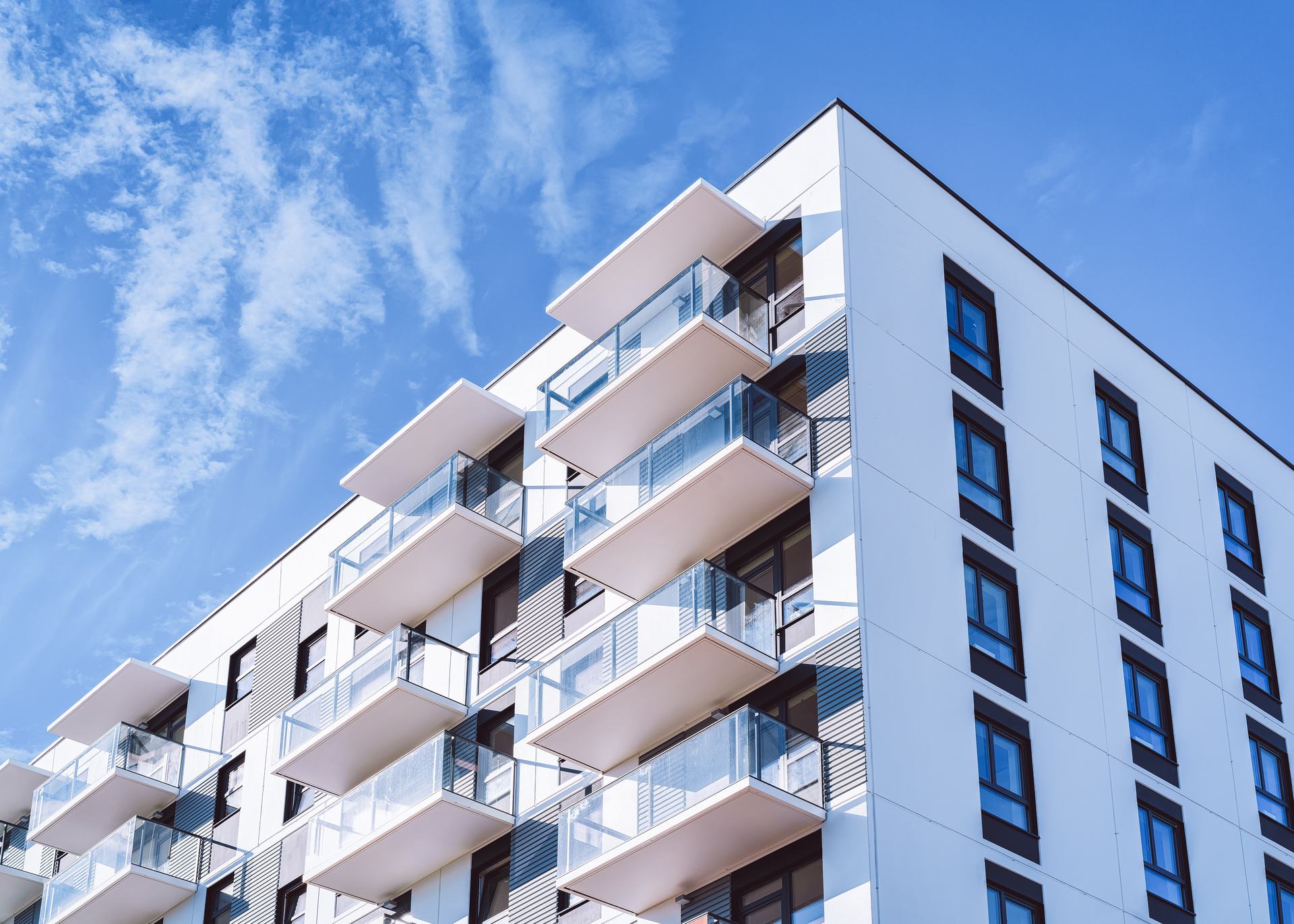 White apartment building with rows of glass balconies against a blue sky