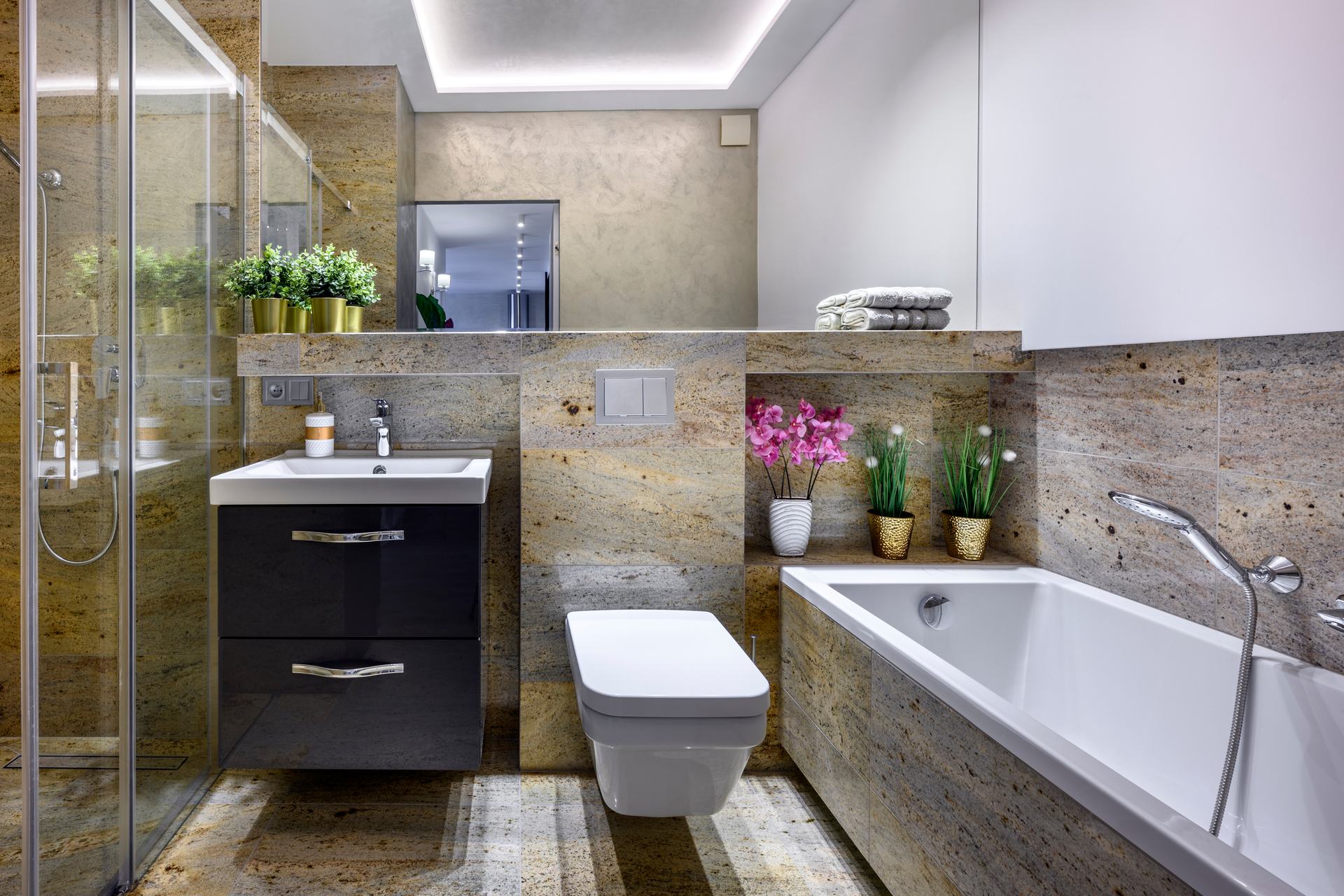 Bathroom with stone-look tiles, a bath and a glass shower, lit by a concealed LED strip around the ceiling